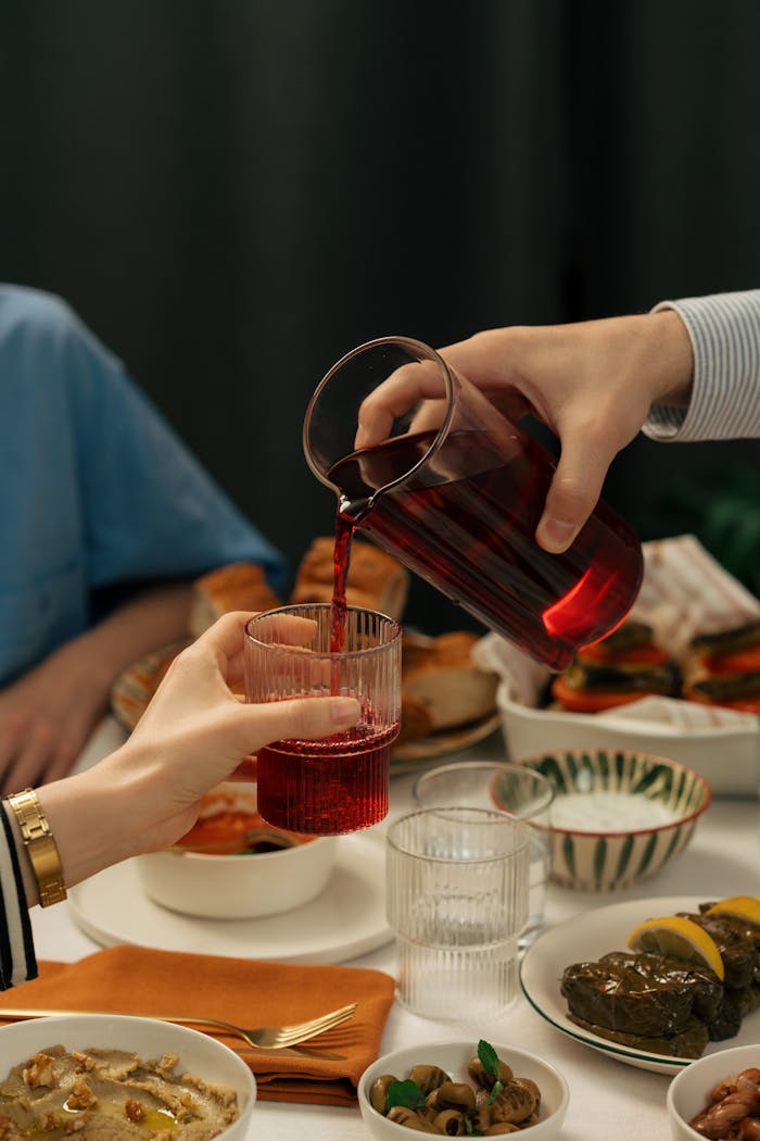 Hands pouring red juice during a Middle Eastern feast, symbolizing togetherness and culture.